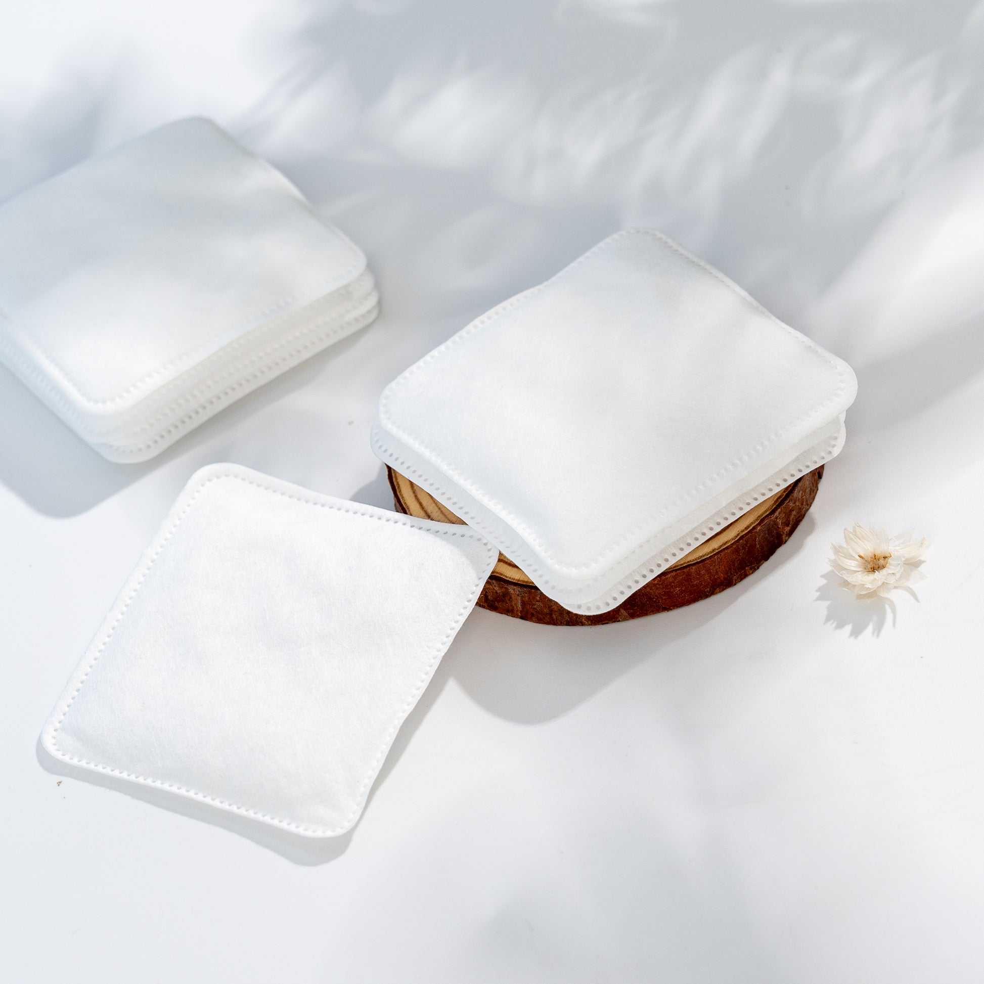 White square cushions on a white surface with a small wooden bowl and flower.